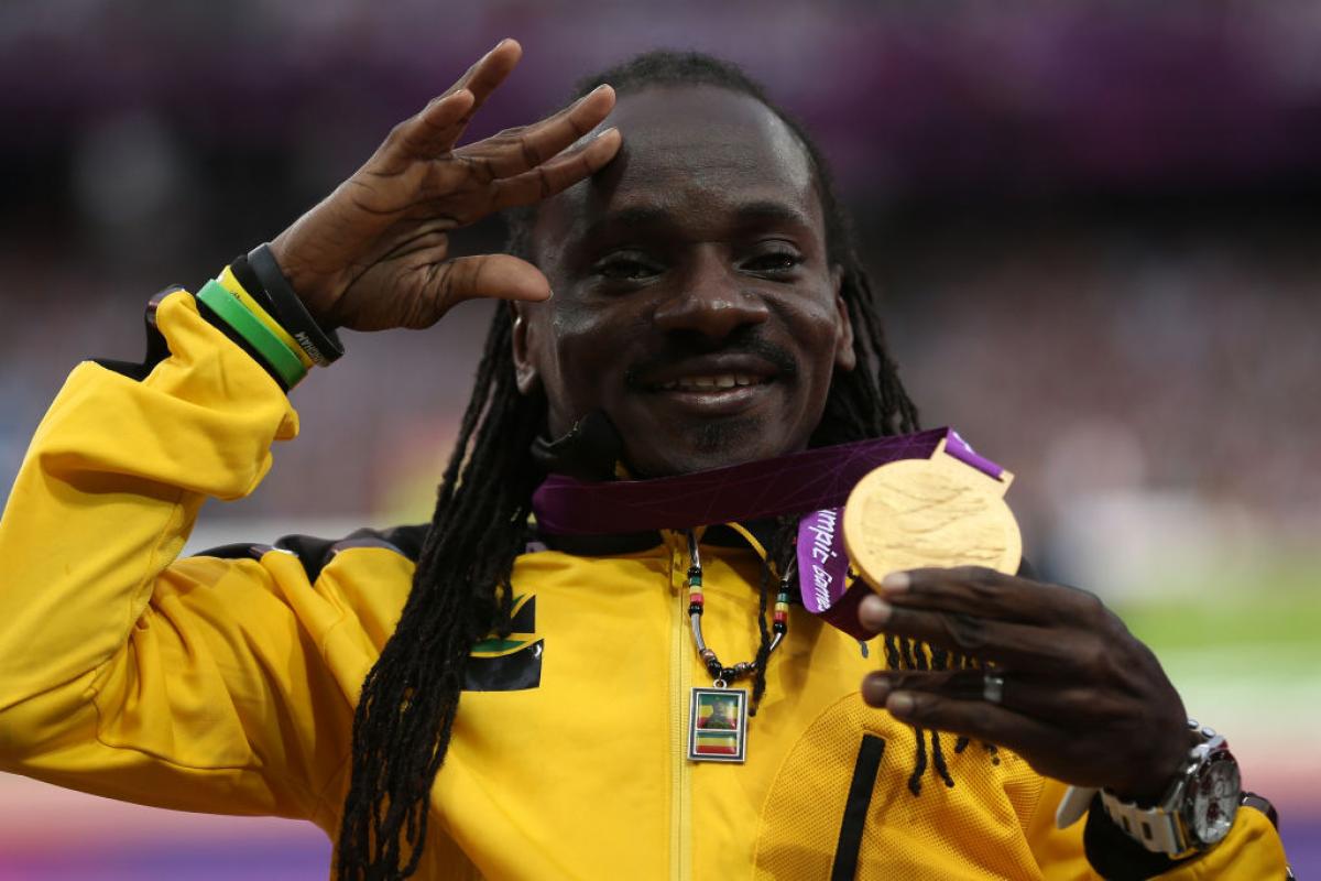 Jamaica's Alphanso Cunningham holds up his gold medal in the men's javelin throw F52/53 and waves with his other hand while posing for photos on the London 2012 podium.