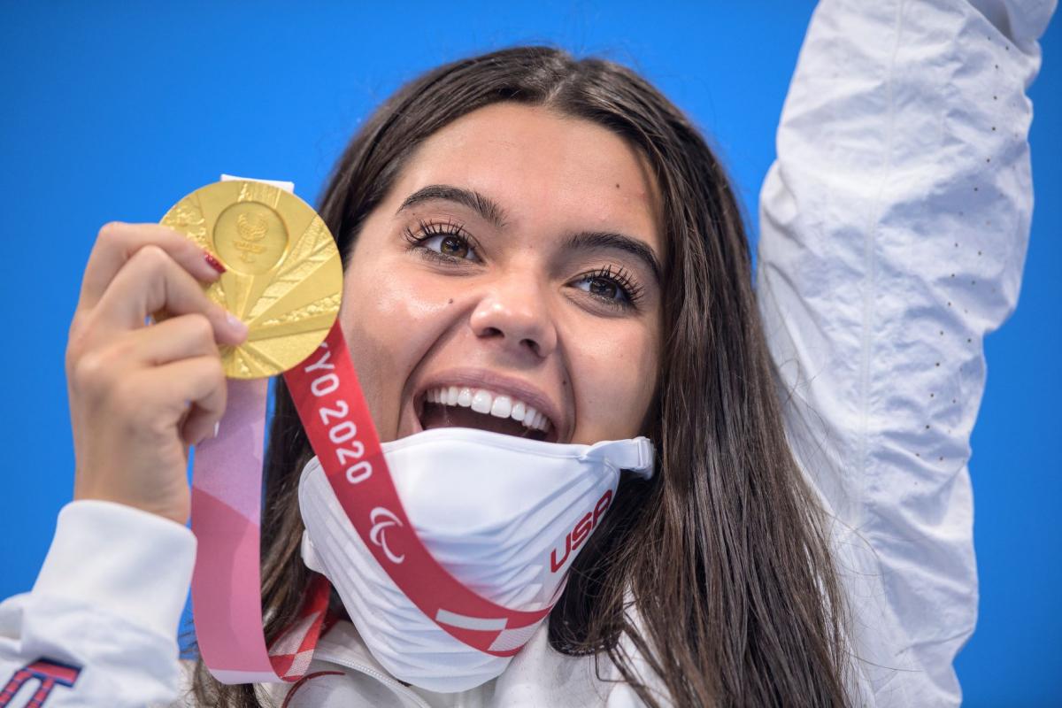 Anastasia Pagonis smiles widely as she holds up her gold medal and raises her other arm in celebration at Tokyo 2020.