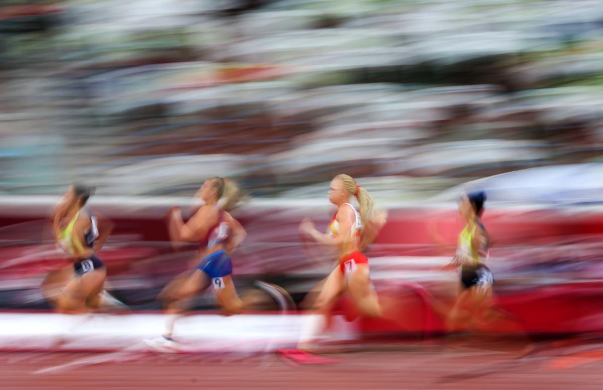 A blurred image of four women competing in an athletics track