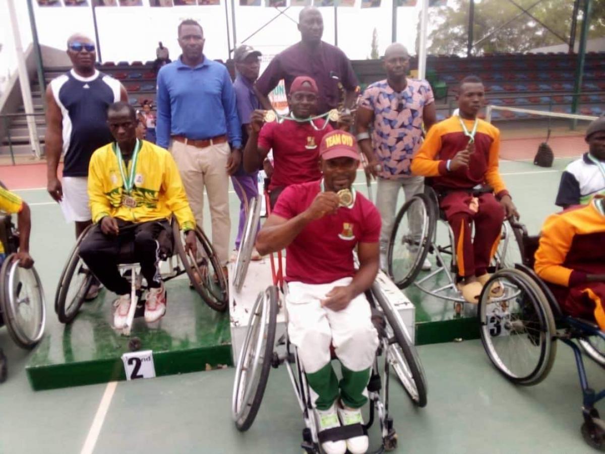 A group of wheelchair tennis players with medals on the podium and next to it.