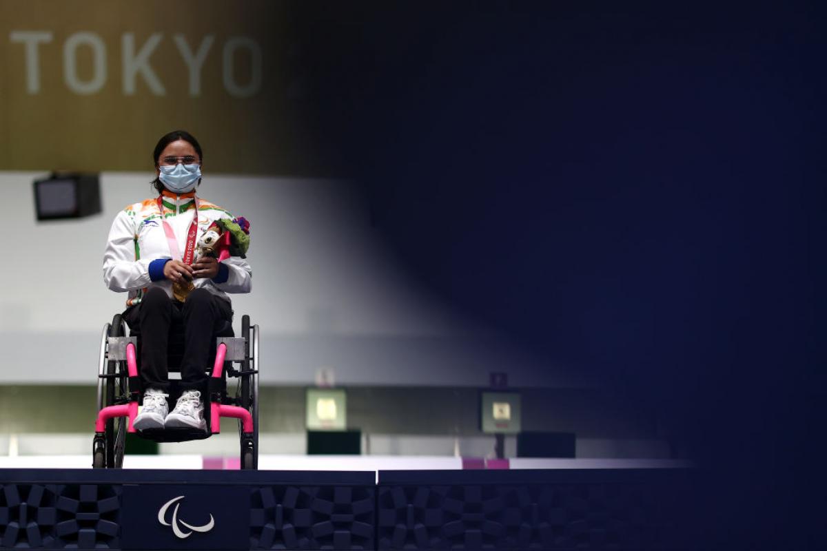 Avani Lekhara sits in her wheelchair on the Tokyo 2020 podium with a gold medal around her neck.