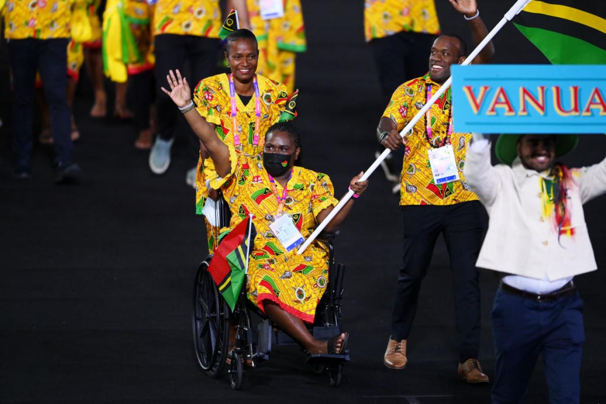 A woman in traditional clothes and in a wheelchair carries the Vanuatu flag in an athlete's parade.