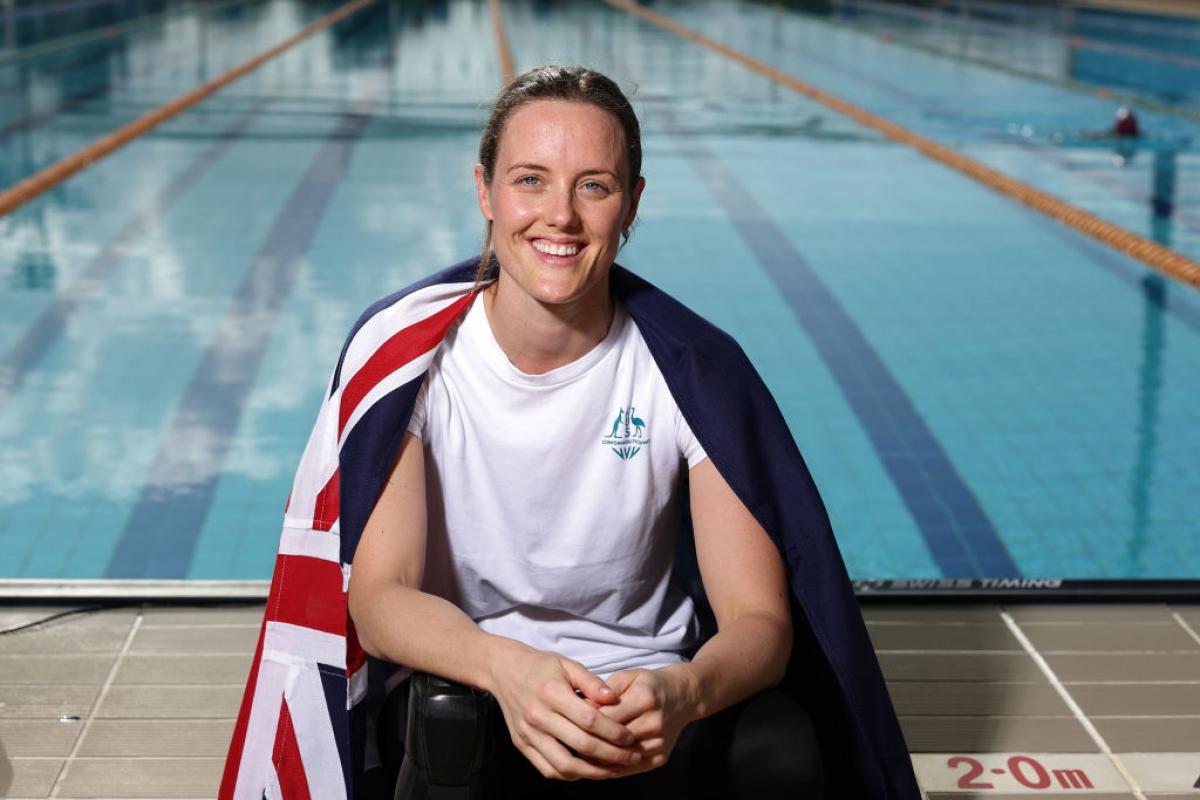 A woman with the Australian flag on her shoulders and a swimming pool in the background