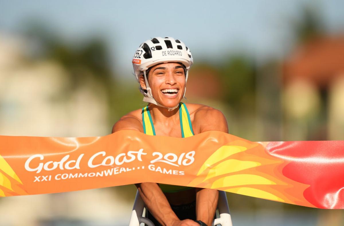 A female wheelchair racer crossing a finish line and smiling