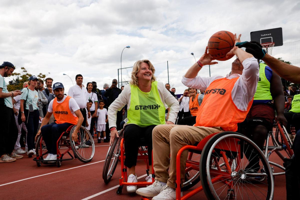 One woman and two men try out wheelchair basketball surrounded by spectators.