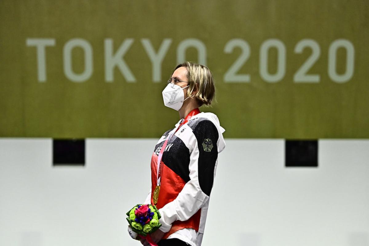 Image of a female Para shooter after winning gold, looking at the German national flag on the podium