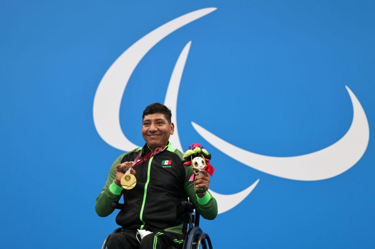 Image of a male Para swimmer in the podium with his gold medal and his flowers