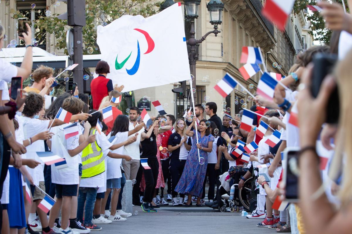 Many people wave the French flag to welcome a woman carrying the Paralympic flag