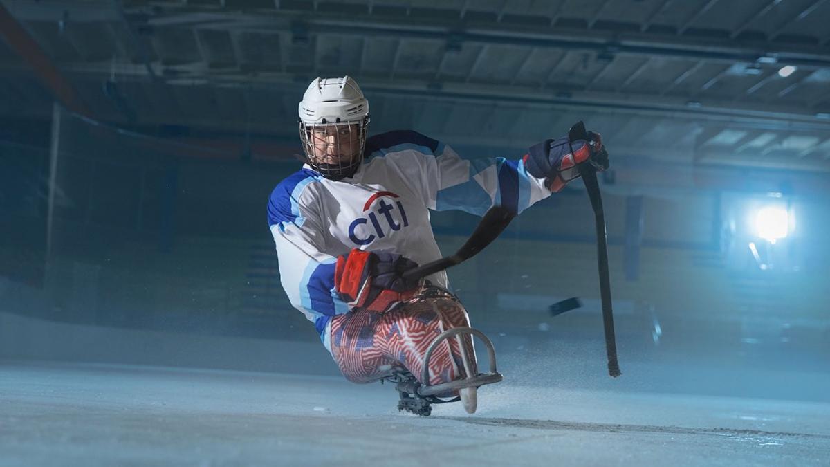 A female Para ice hockey player taking a shot alone in an ice rink