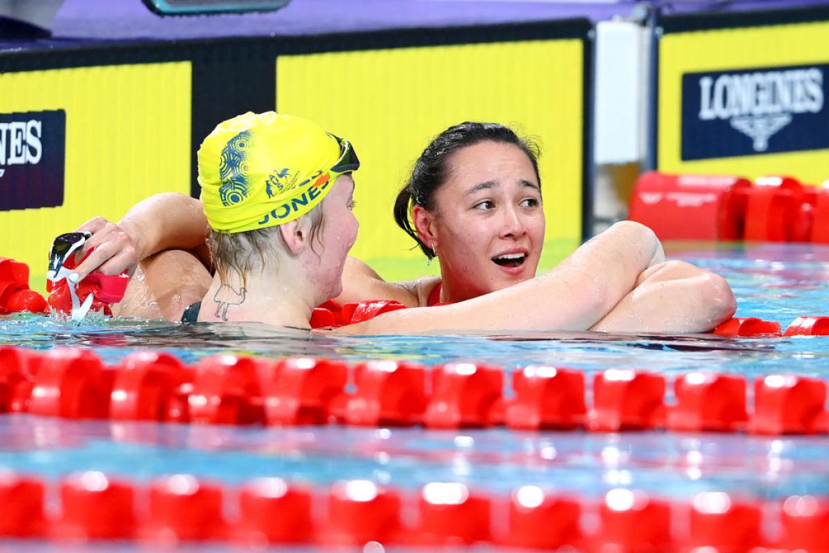 A female swimmer embracing another female swimmer looking surprised in the pool