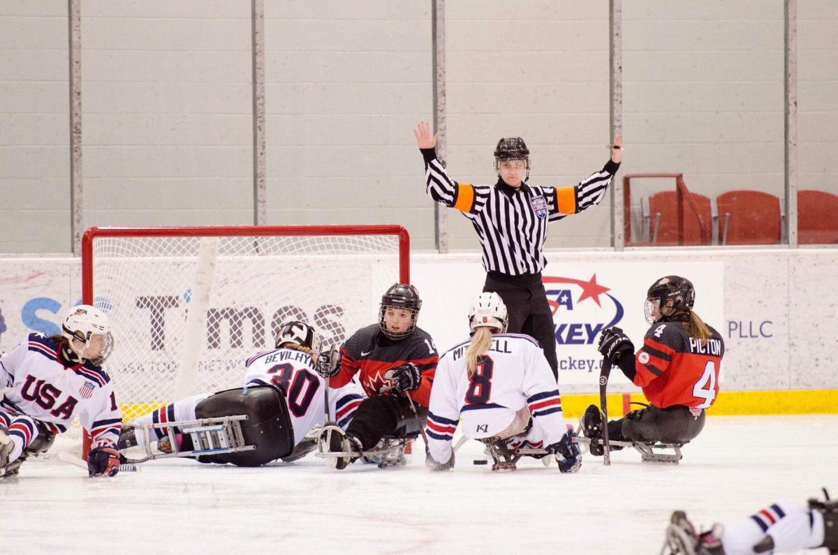 A female Para ice hockey official raising her arms in front of five female players