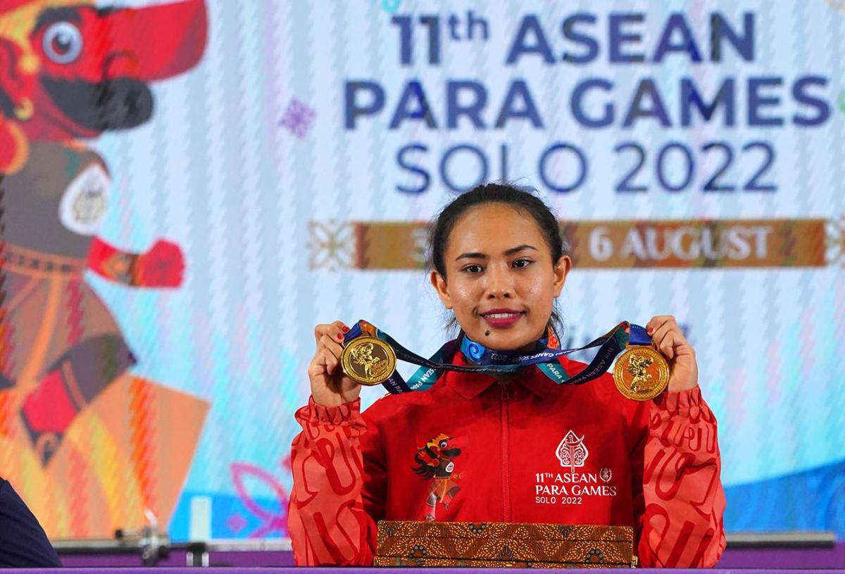 A woman showing her gold medals with a backdrop of the 11th ASEAN Para Games
