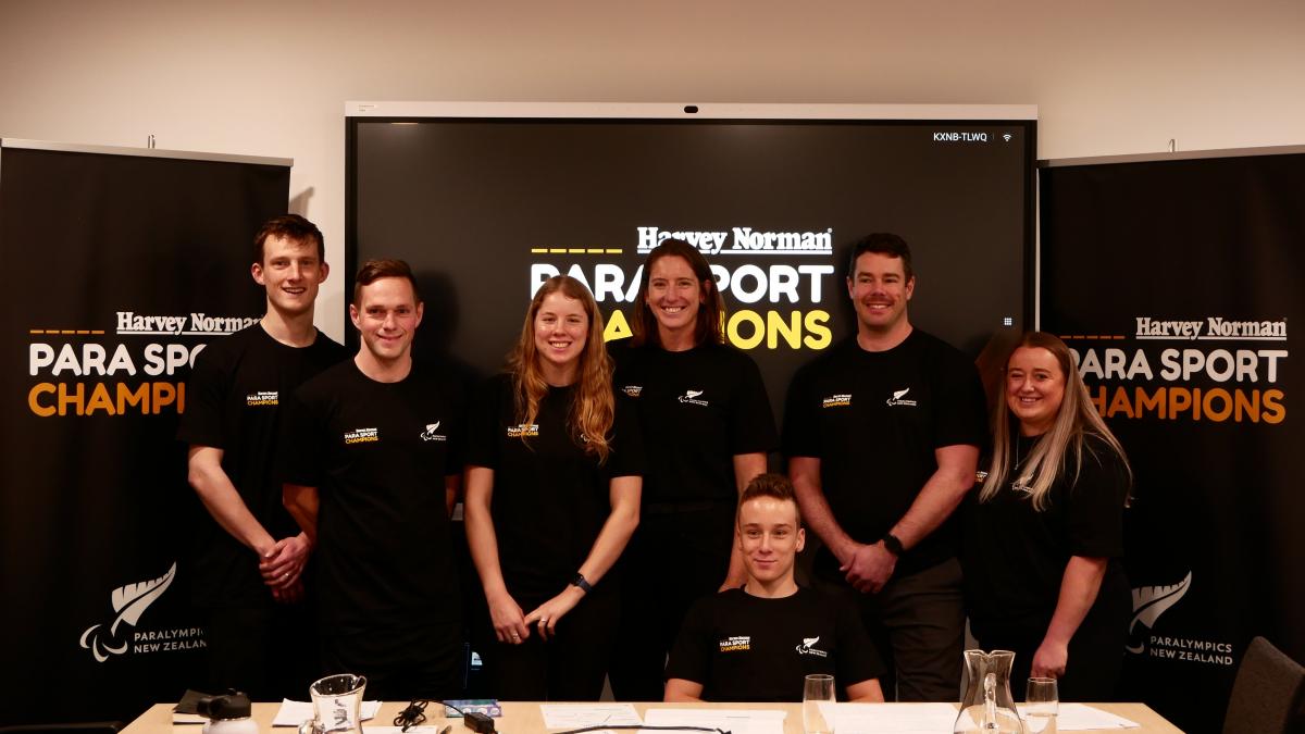 Seven Para athletes pose for a photograph in front of a screen and posters with the words "Harvey Norman Para Sport Champions."
