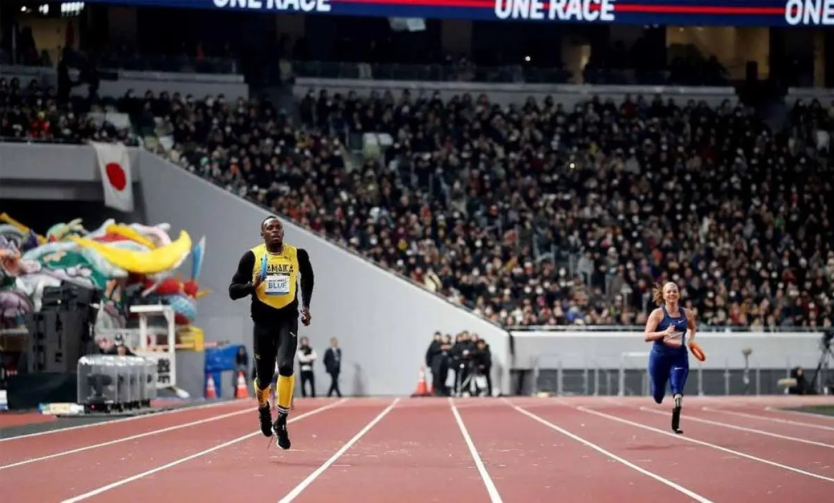 A male sprinter and a female sprinter run on the track of a packed stadium while holding relay batons.