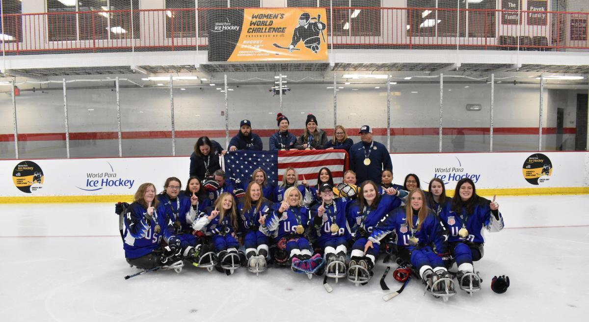 A group of Para ice hockey players and their staff celebrate with gold medals around their necks.
