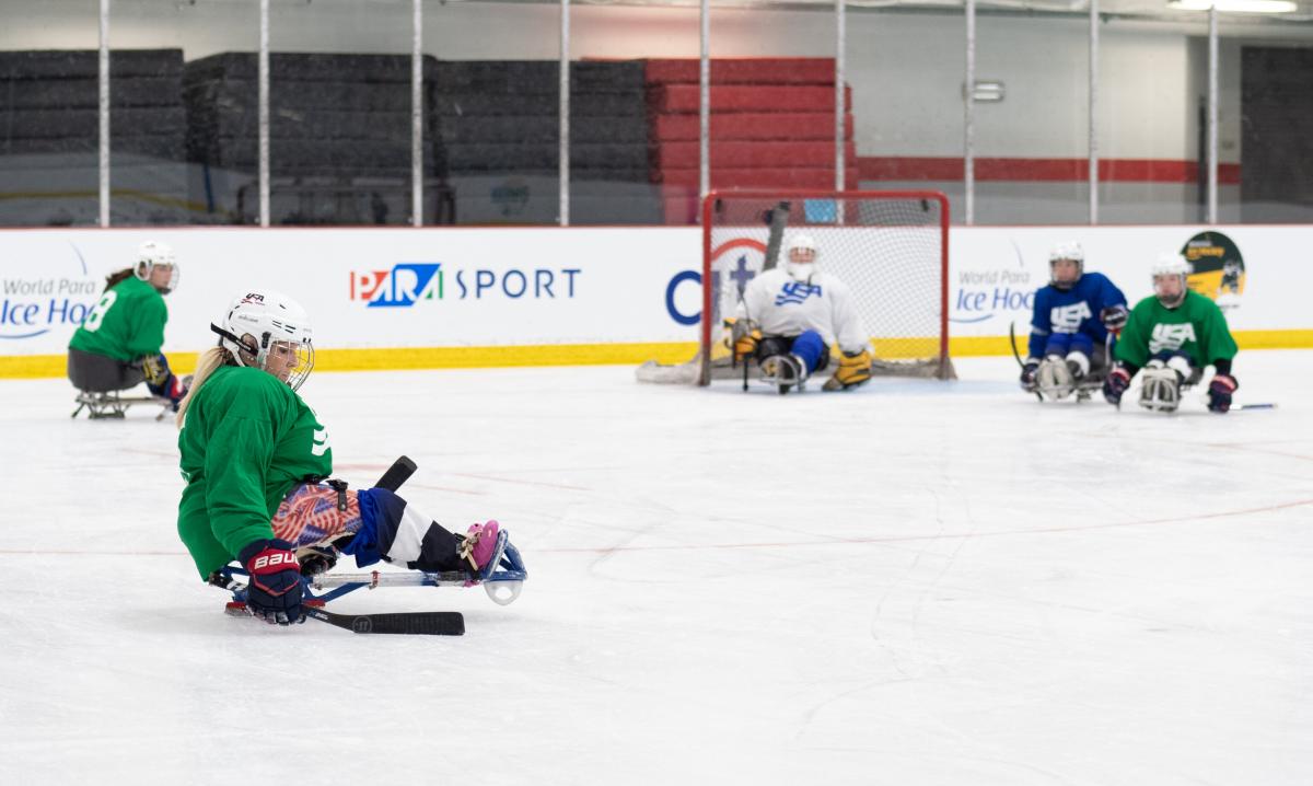 A woman in green jersey and on a sled is preparing herself to shoot the puck.