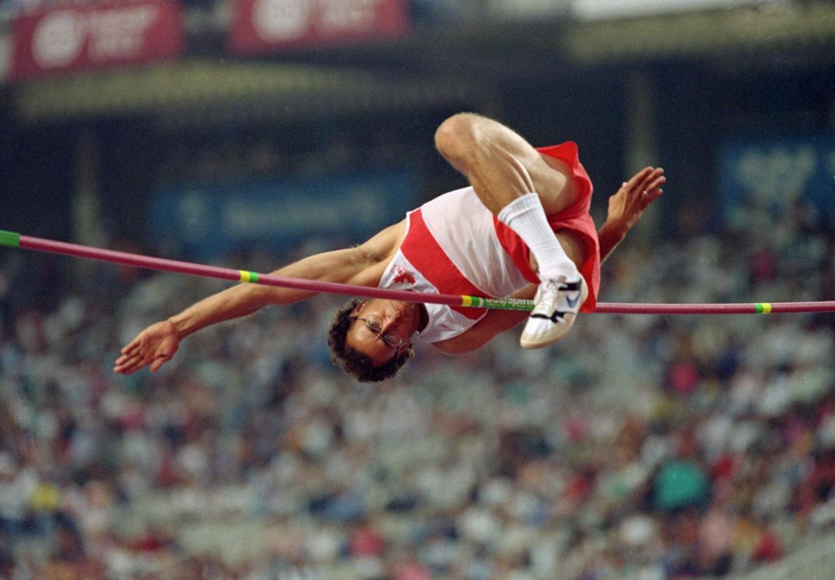 A male athlete jumps over the bar in a stadium full of spectators.