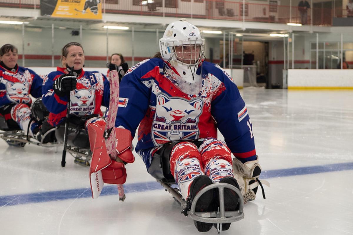 Female Para ice hockey players wearing Great Britain jerseys form a line on the rink.