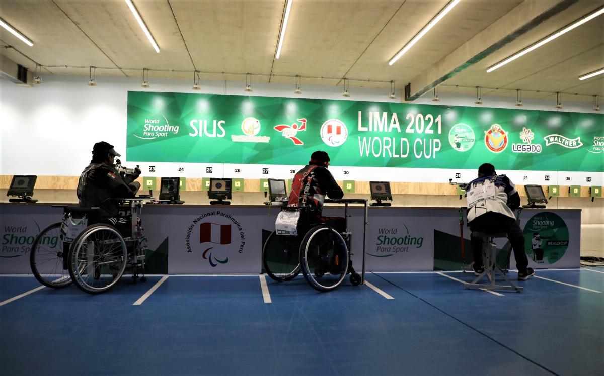Three shooters in wheelchairs competing in an indoor shooting range