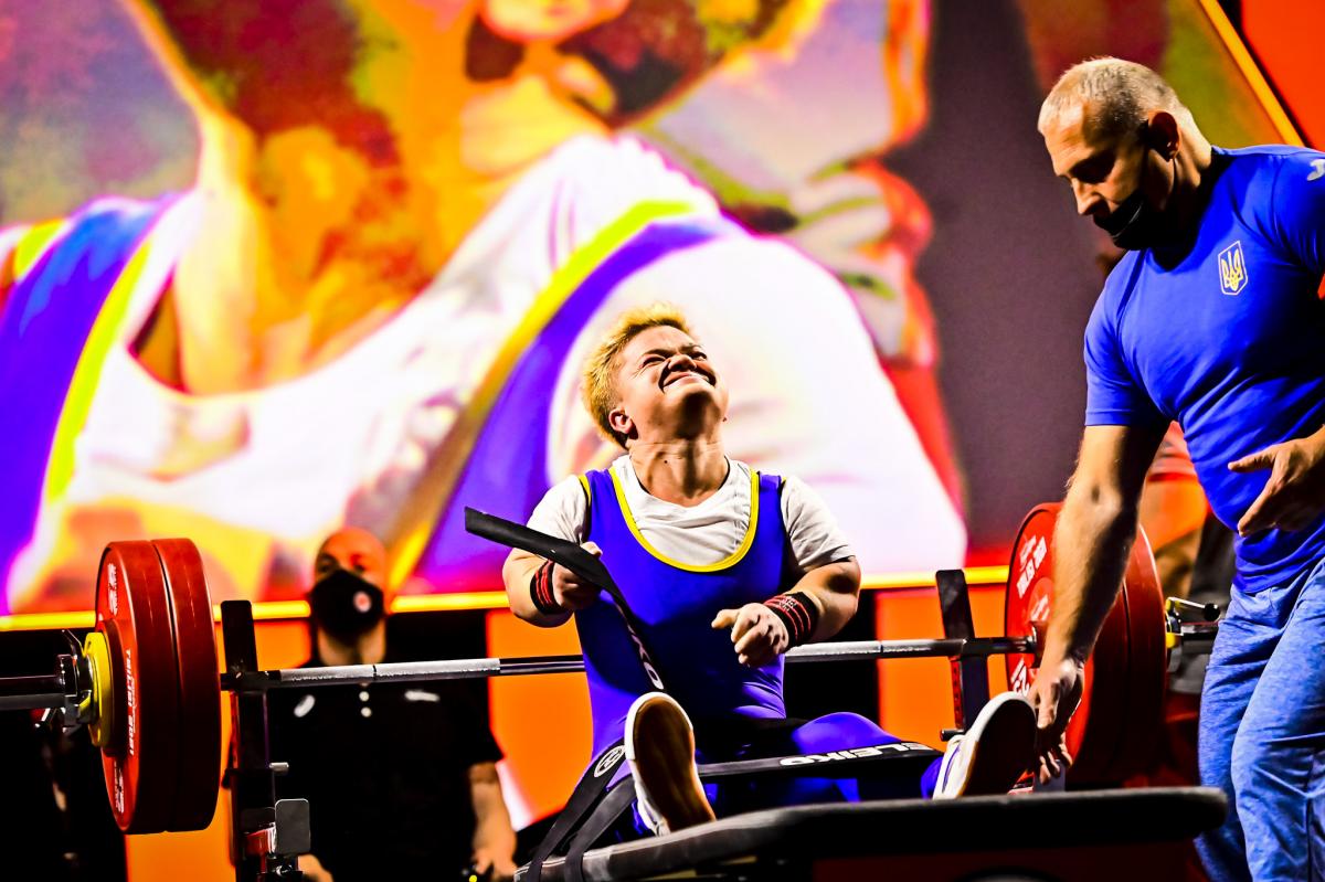 A female Para powerlifter takes off her belt and celebrates after a lift.