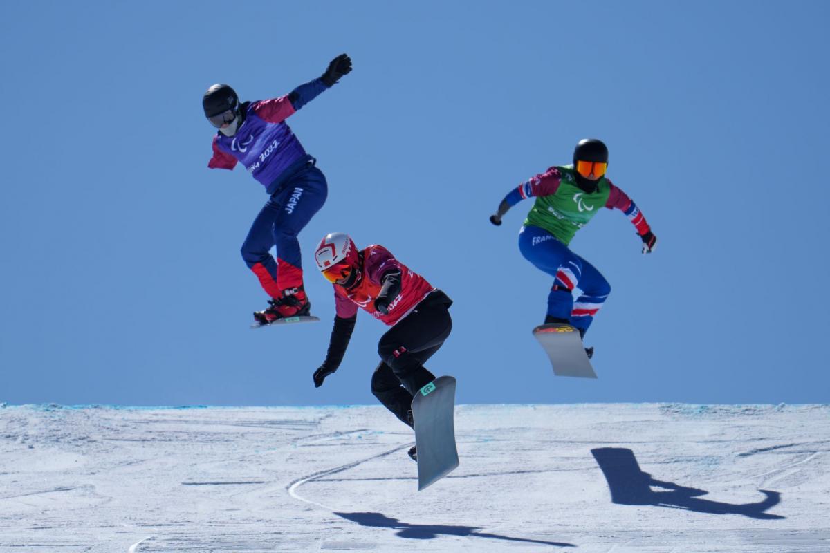 Three male Para snowboarders jump during the snowboard cross race at Beijing 2022.