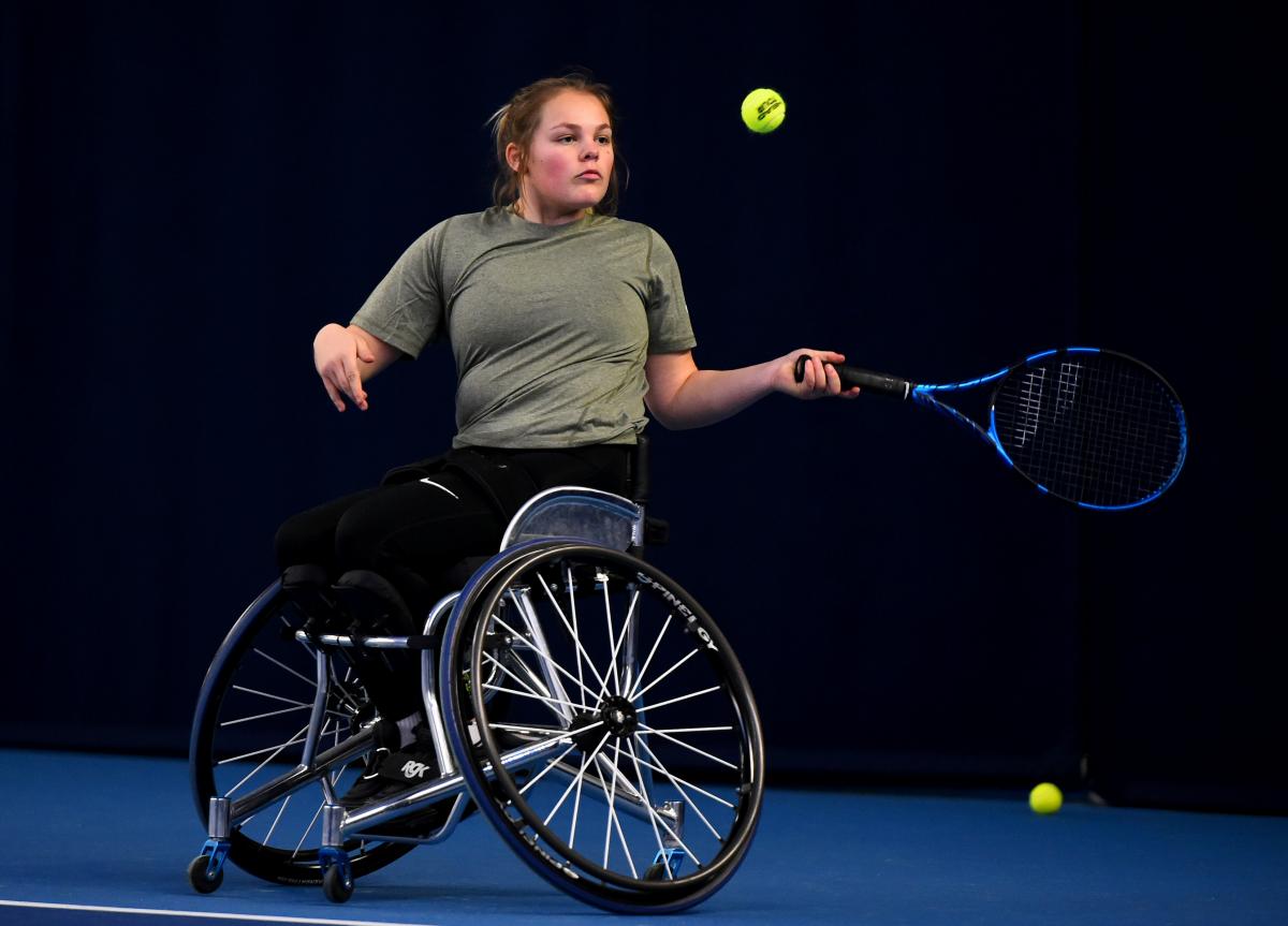 A female wheelchair athlete plays a forehand on a blue court.