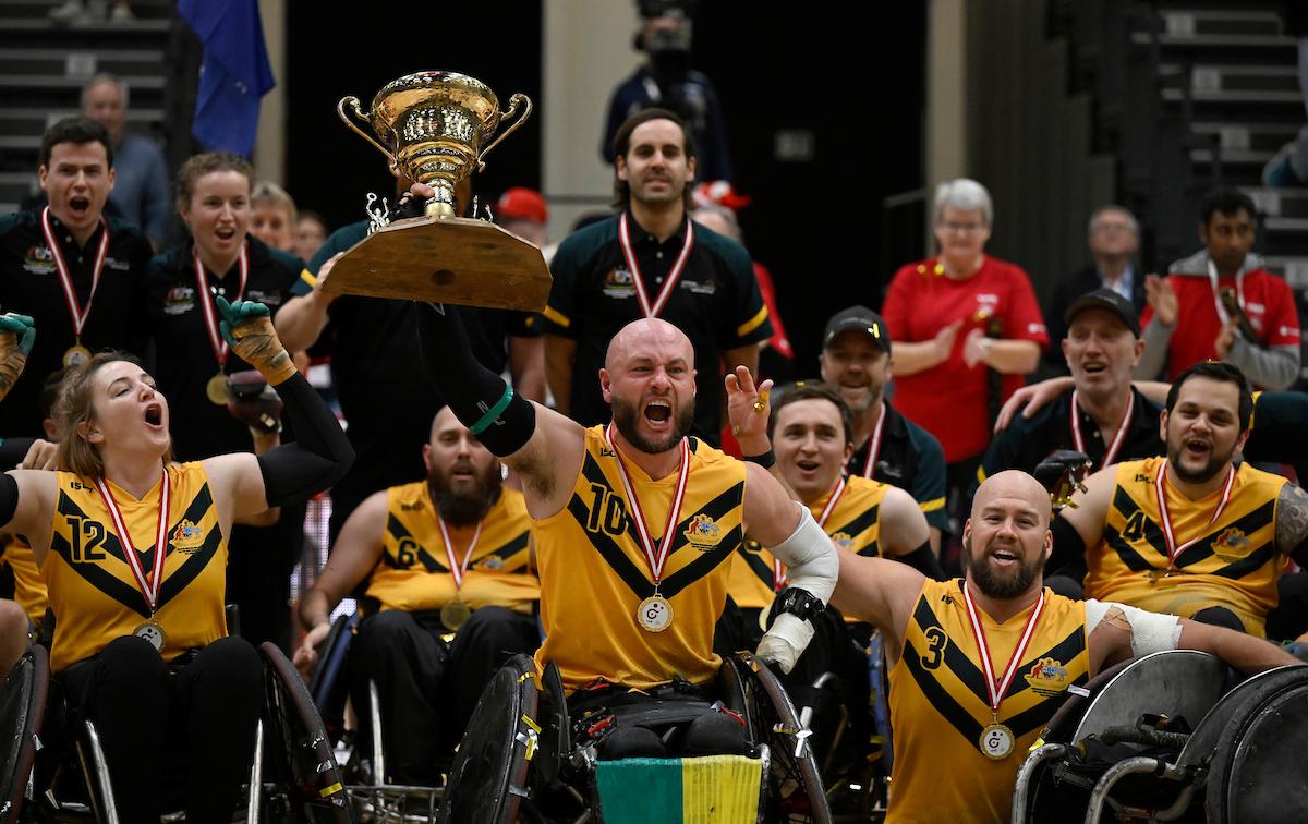 Wheelchair rugby players wearing yellow jerseys celebrate their victory