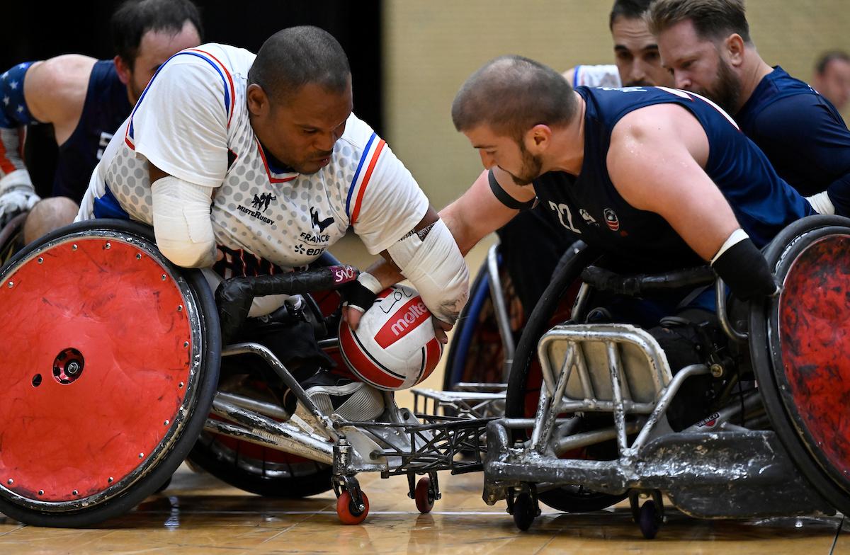 Two wheelchair rugby players reach for a ball