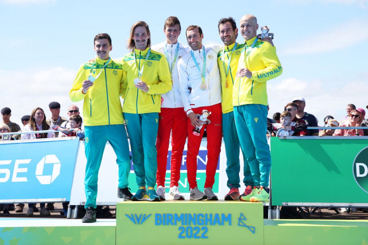 Six male athletes stand on the podium