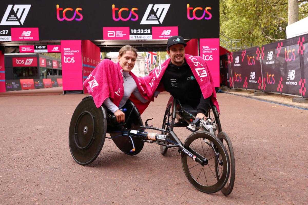 A woman and a man in racing wheelchair racers in front of the finish line of the London Marathon
