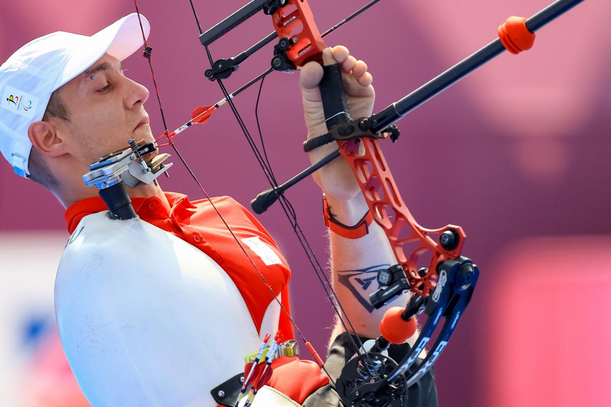 A man holds the bow with his legs and prepares to draw the arrow with his mouth.