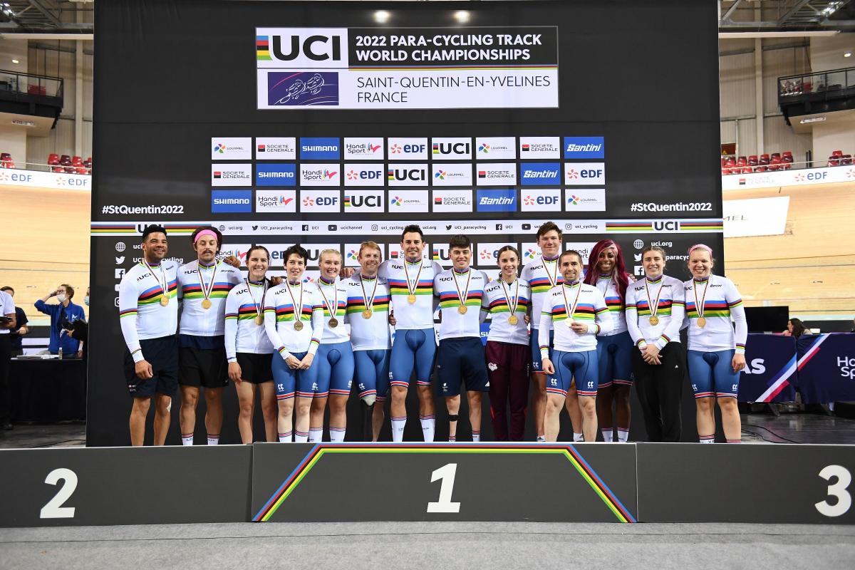 Fourteen British Para cyclists, all with medals, pose for a group picture on the podium.