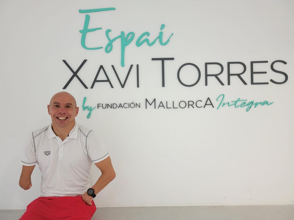 A male athlete smiles in front of the wall with the words "Espai Xavi Torres by Fundacion Mallorca Integra"