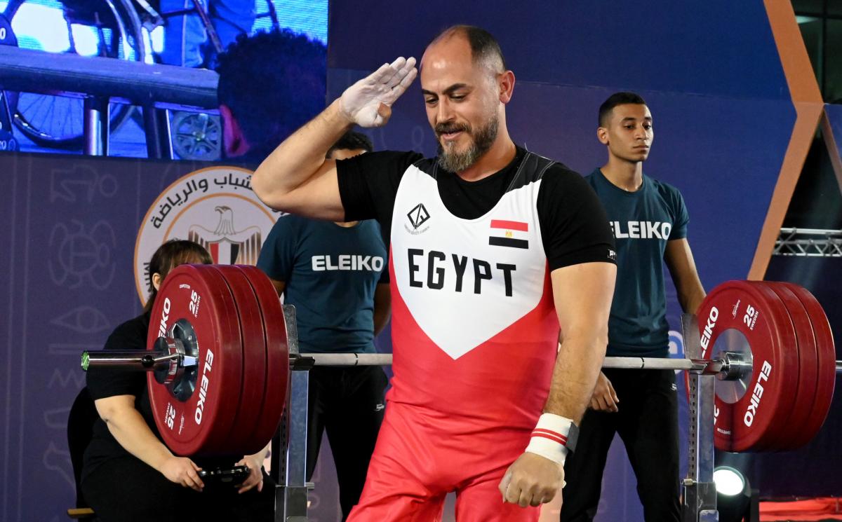 A man salutes with his right arm after lifting weights on a bench press.