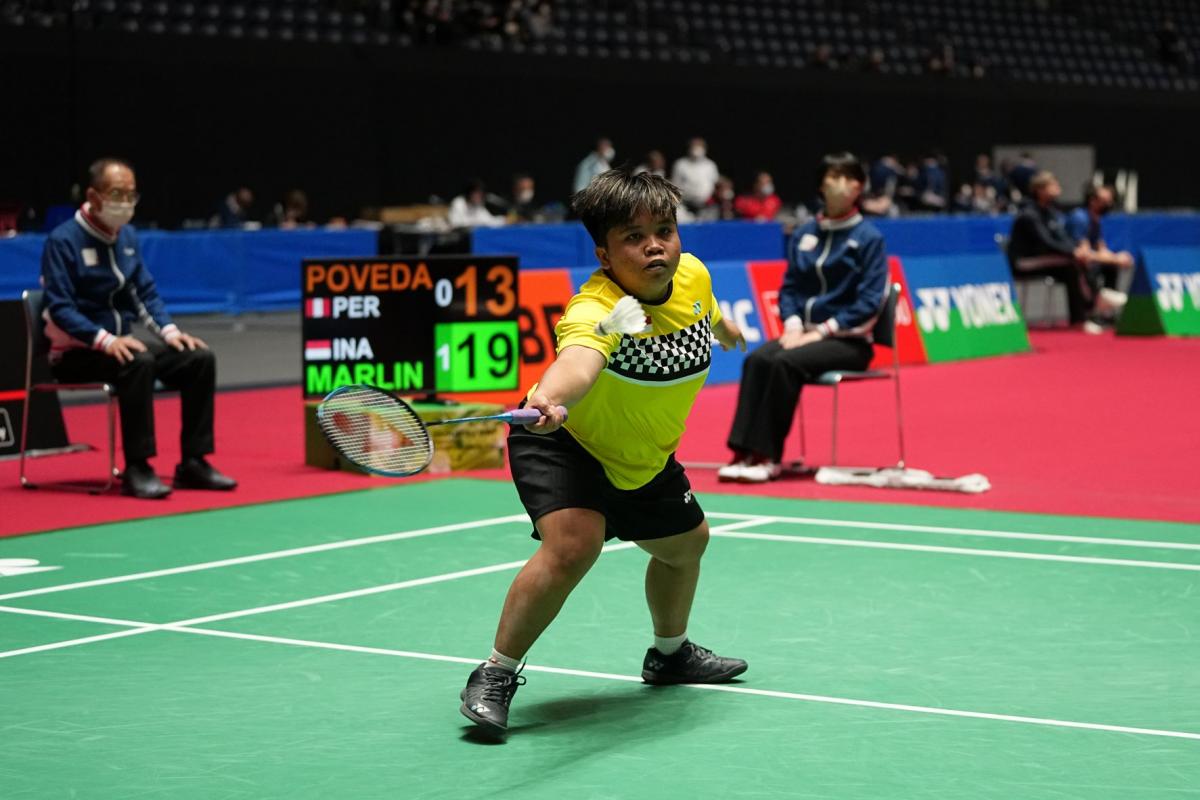 A female athlete holds a racket with her left hand and reaches out for the shuttle.