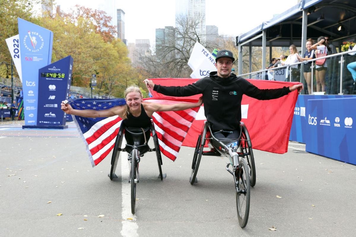 A female wheelchair racer with the USA flag and a male racer with the Swiss flag in front of a marathon finishing line