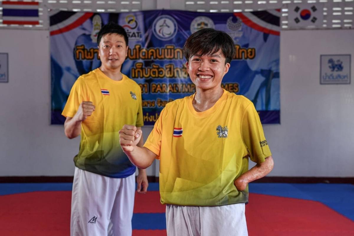 A woman with a left arm missing near the wrist and a man pump their right fists while standing on a training mat.