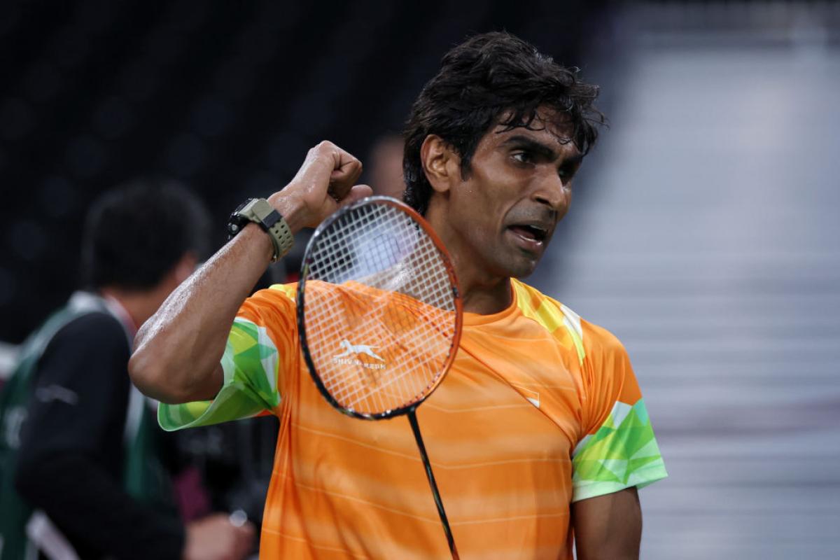 A male athlete pumps his right fist, while holding a badminton racket with the other hand