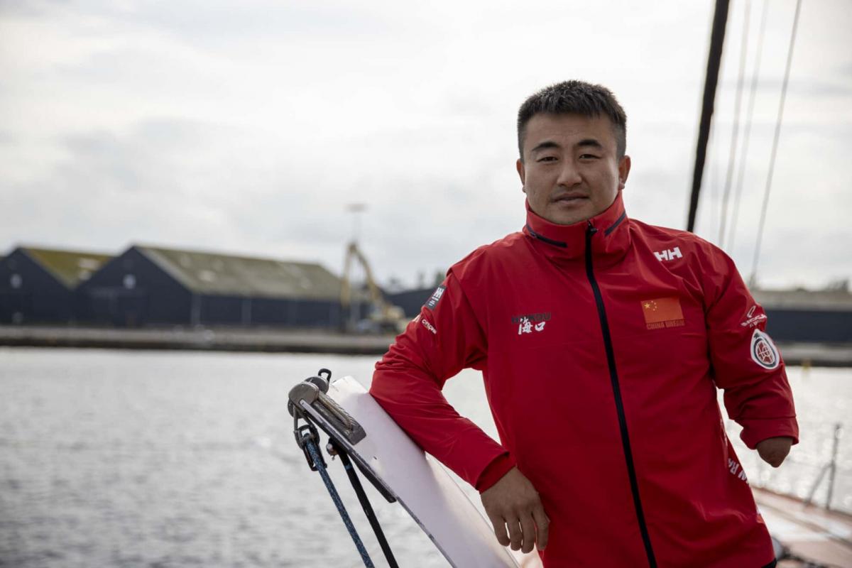 A male sailor missing his left arm below the elbow stands on a sailing yacht at sea.