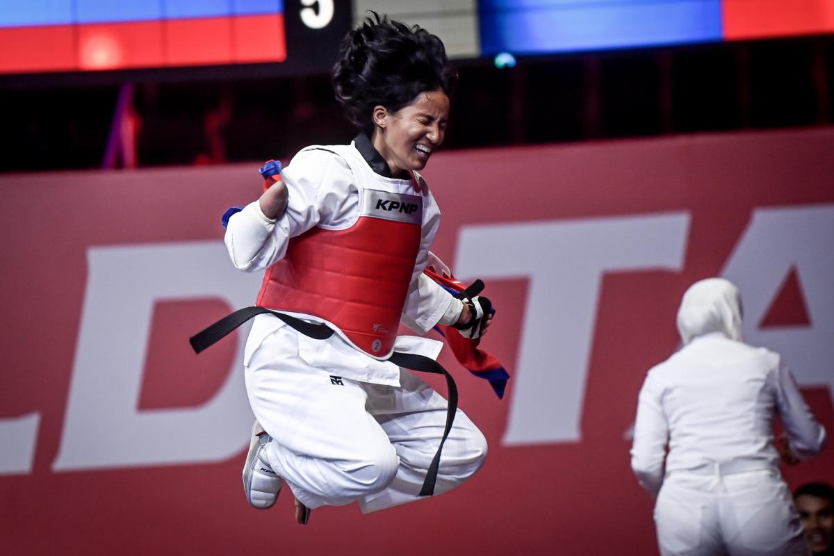 A female Para taekwondo athlete jumps with joy while holding a Nepalese flag after winning the final fight.