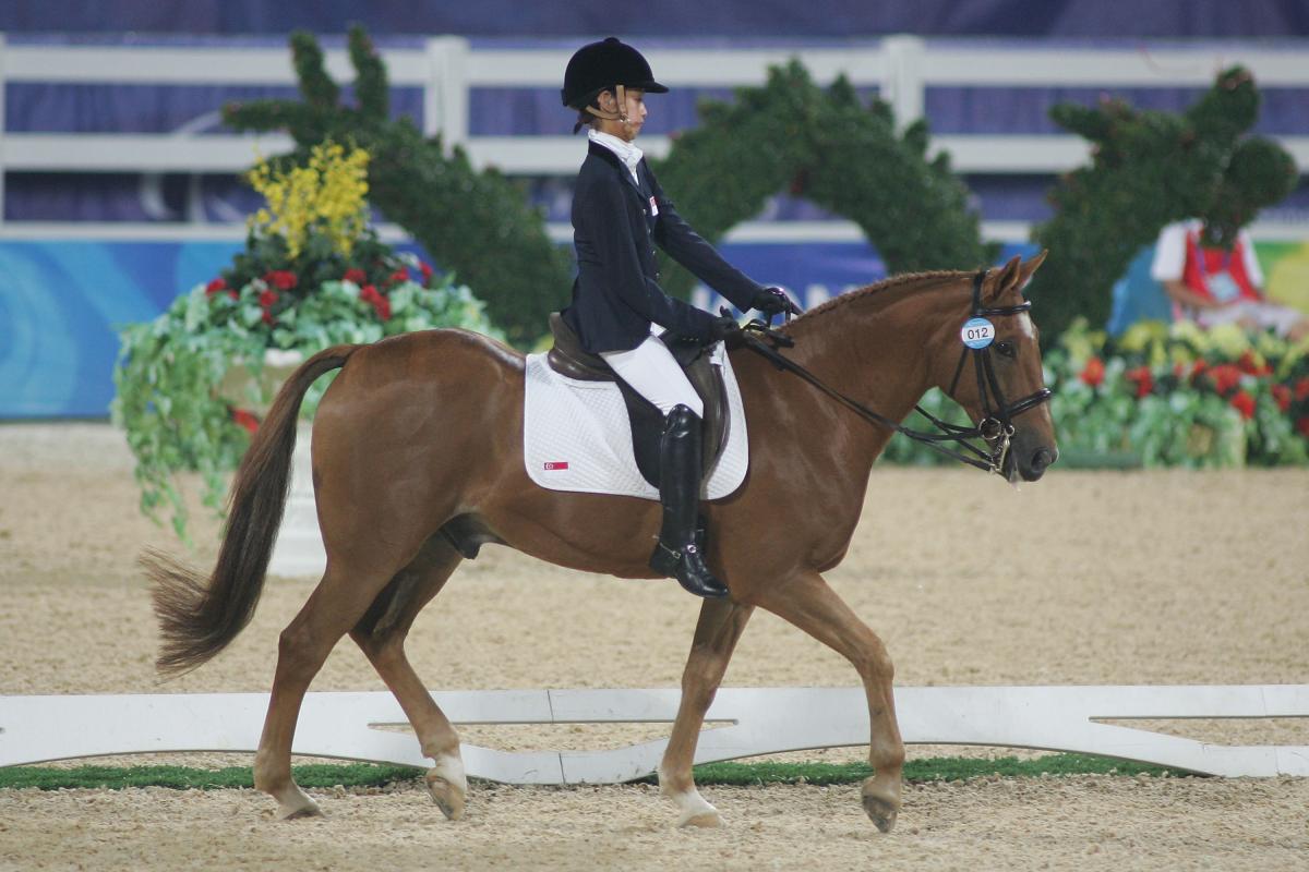 A female athlete rides a horse, walking calmly, during competition.
