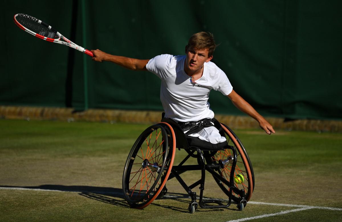 A male wheelchair tennis player extends his arms after returning the ball.