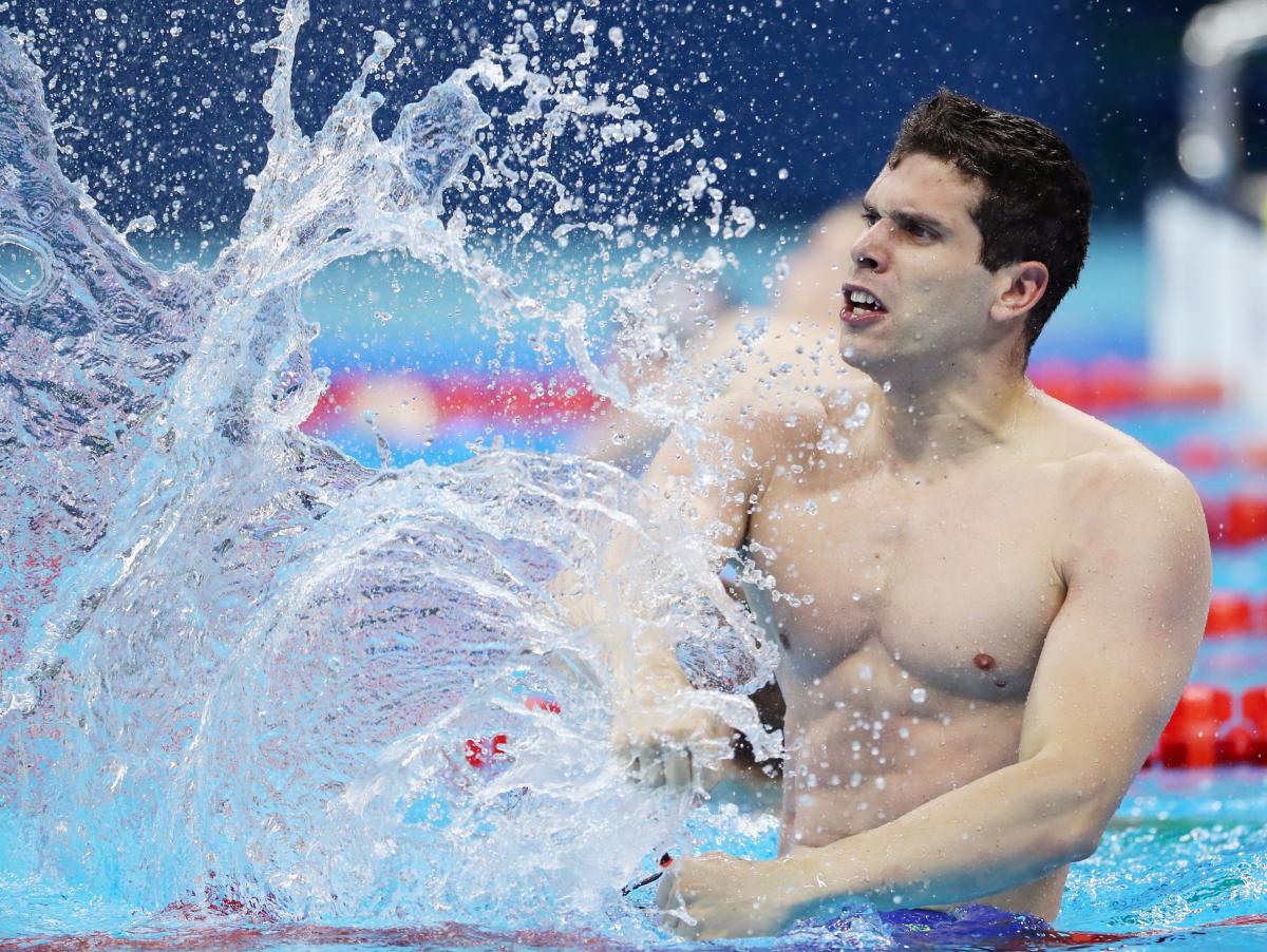A male swimmer creates a big splash as he hits the water with his right fist after the finish of the race.