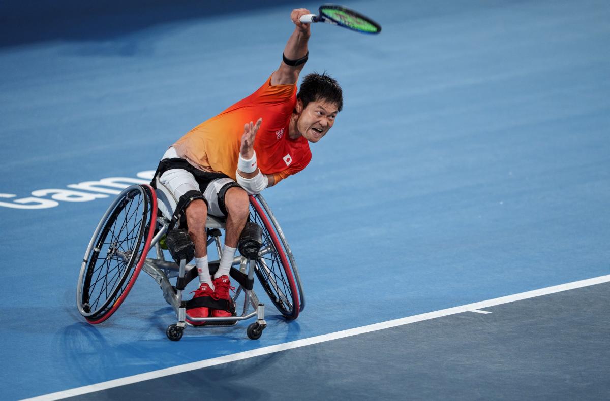 A male wheelchair tennis player holds the tennis racquet with his right hand