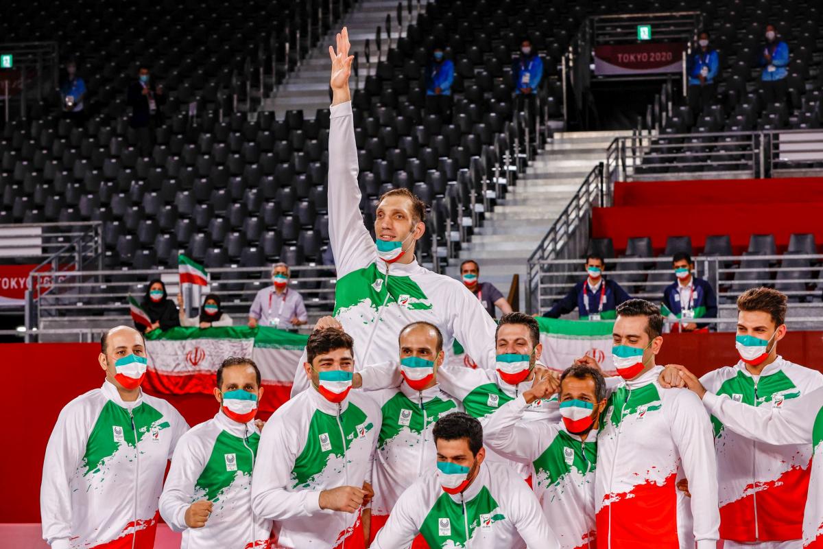 Male sitting volleyball athletes in national uniforms and masks featuring the Iranian flag pose for a photo as they wait for the medal ceremony at Tokyo 2020.