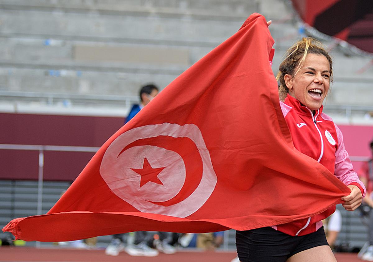 A short-stature woman celebrating with the flag of Tunisia