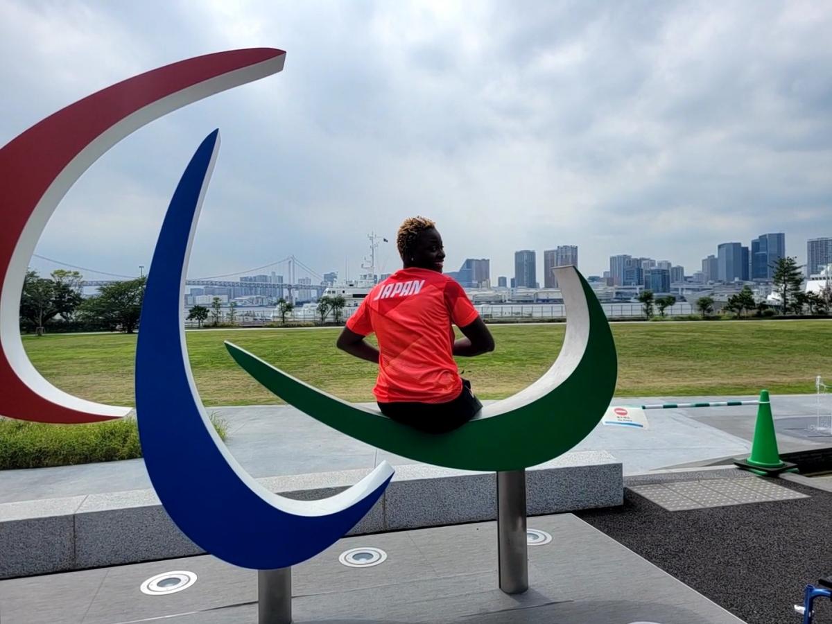 A female athlete wearing Japan's red uniform sits on the Three Agitos monument.