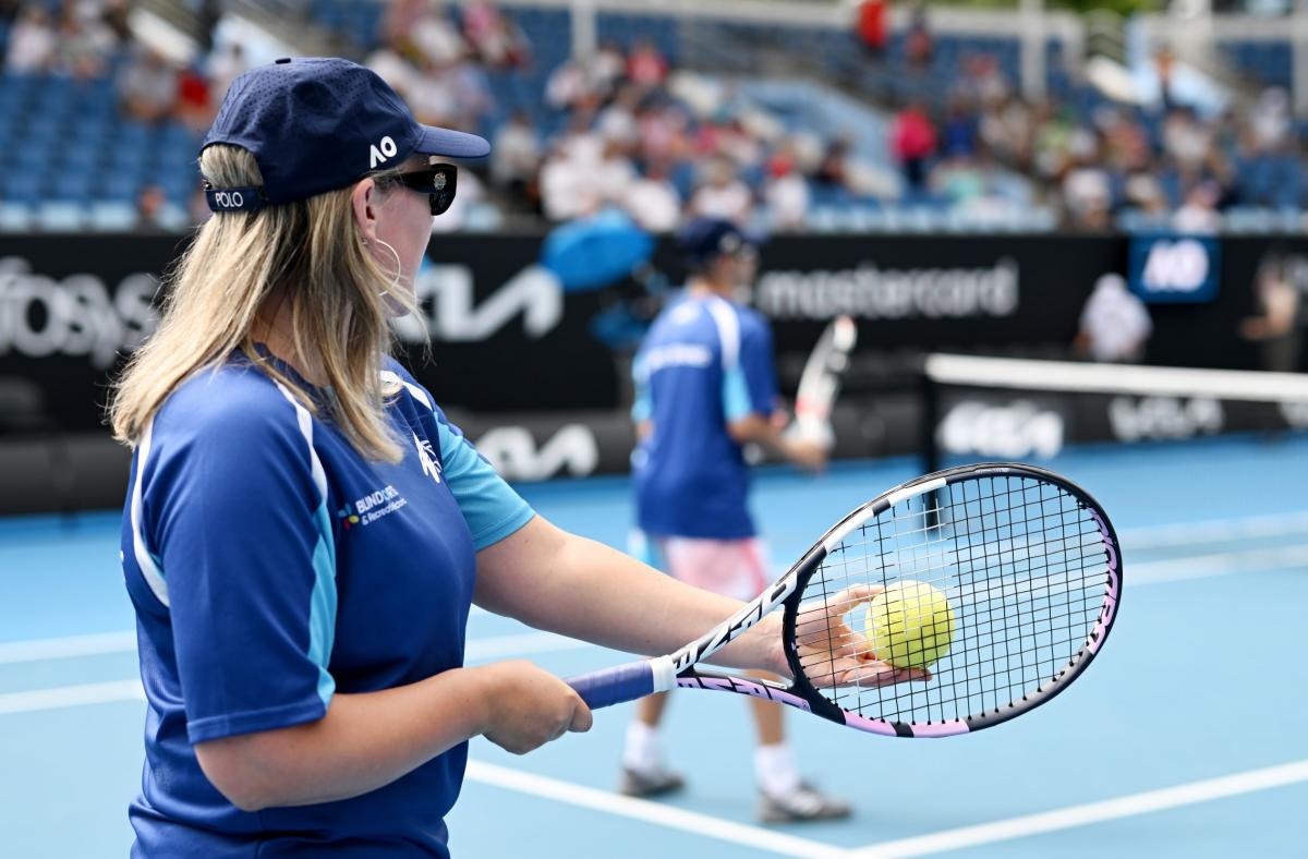 A female athlete prepares to serve a yellow ball used in blind and low vision tennis