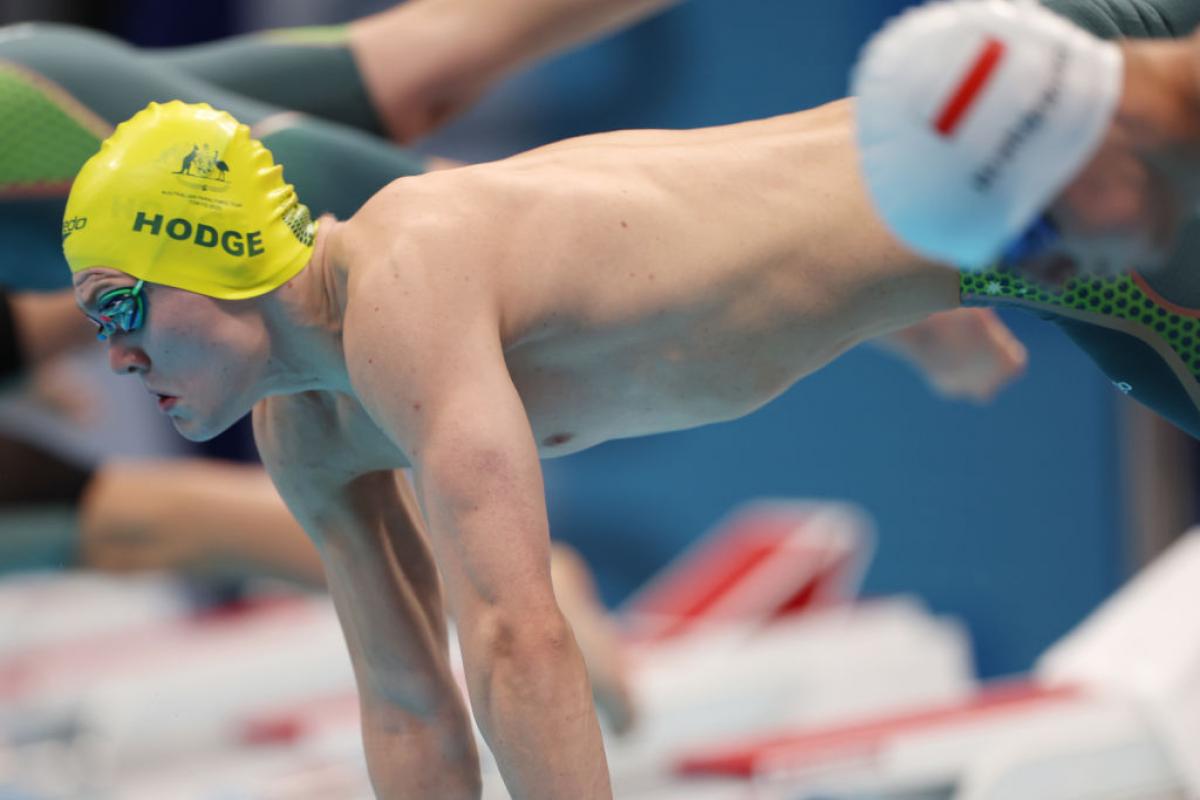 A male swimmer with a cap of Australia jumping in the water with another male swimmer in the foreground