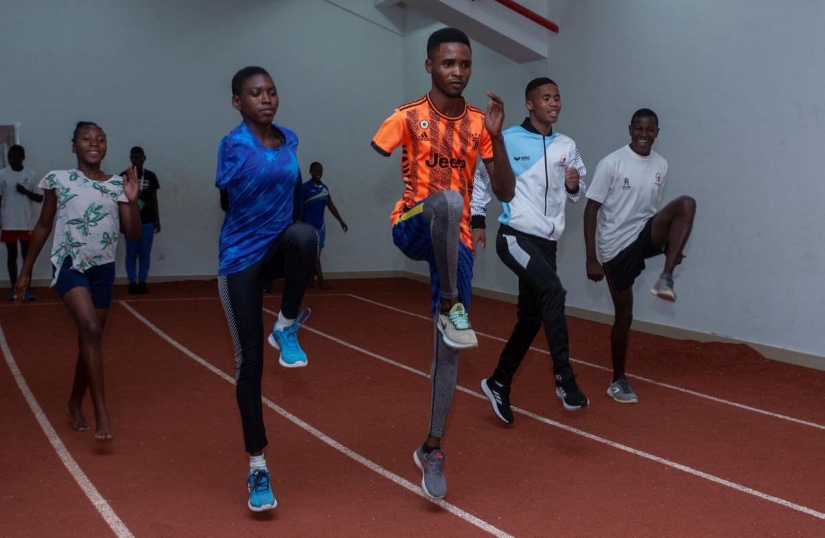 Five African athletes train, doing upward kicks, on an indoor track.